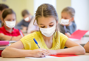 girl in mask writing in school