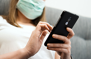 woman in mask using phone at home